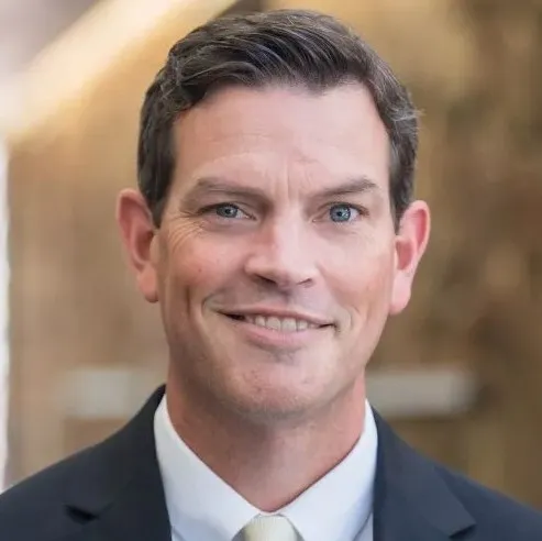 Headshot of Kevin Laudner in a black suite against a gold background